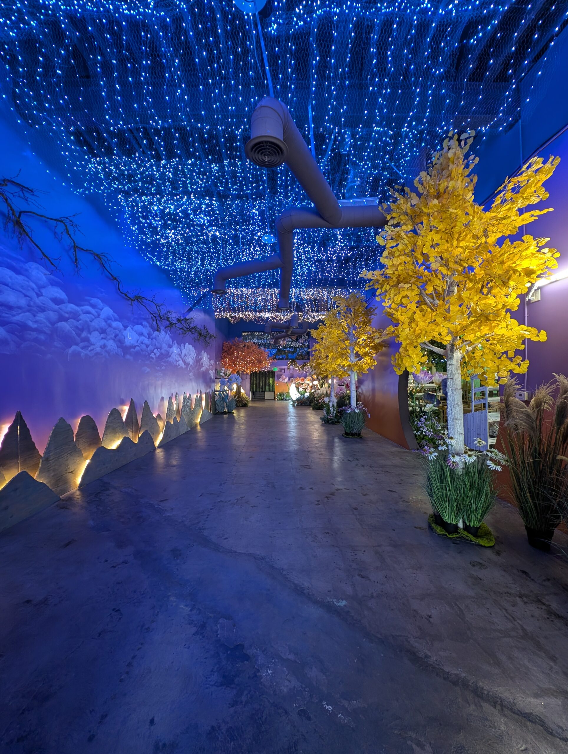 Blue light installation and yellow trees inside Happy Humble Hub
